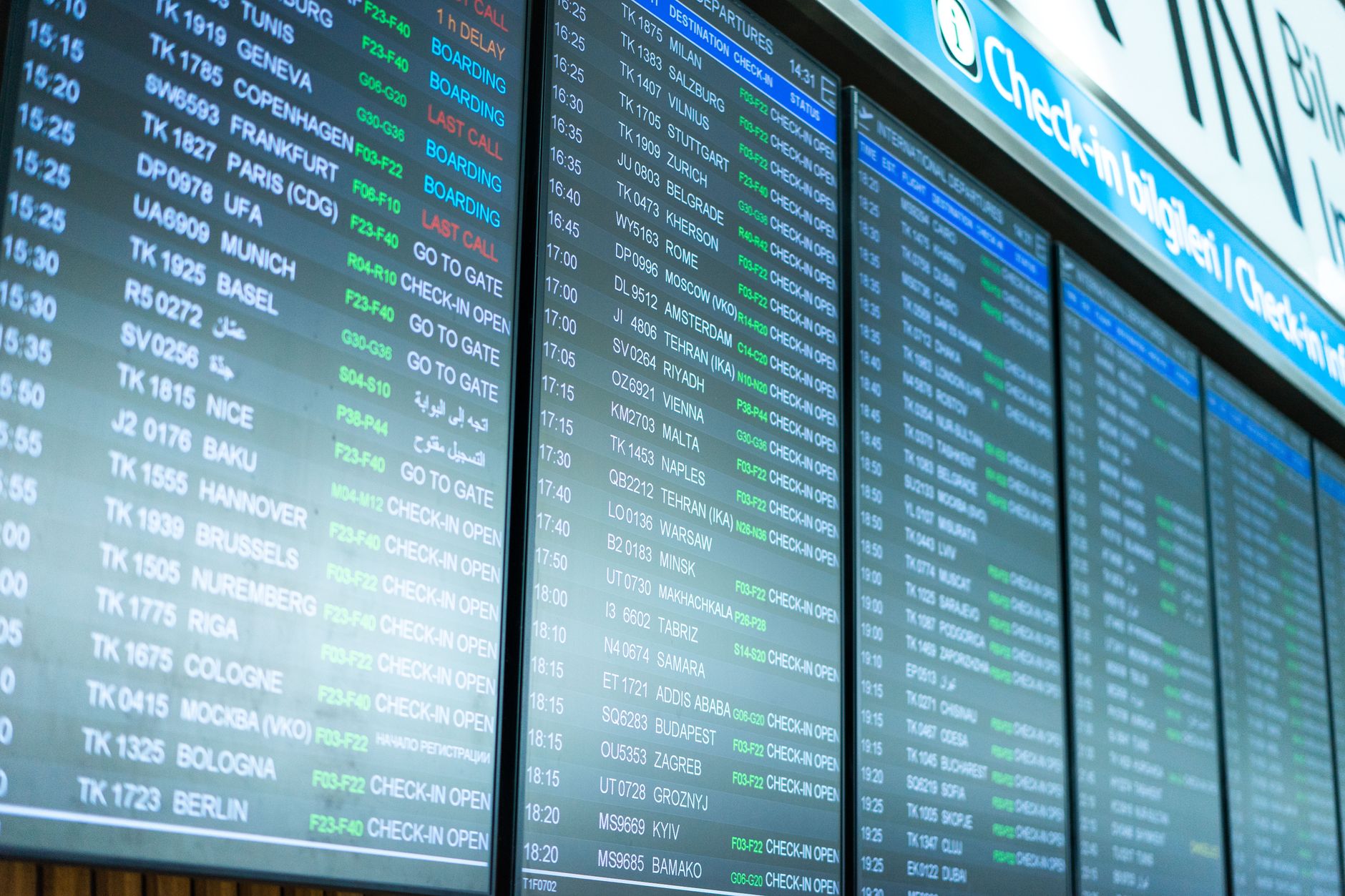 Airport departure board displaying flight times and gate numbers with travelers standing beneath