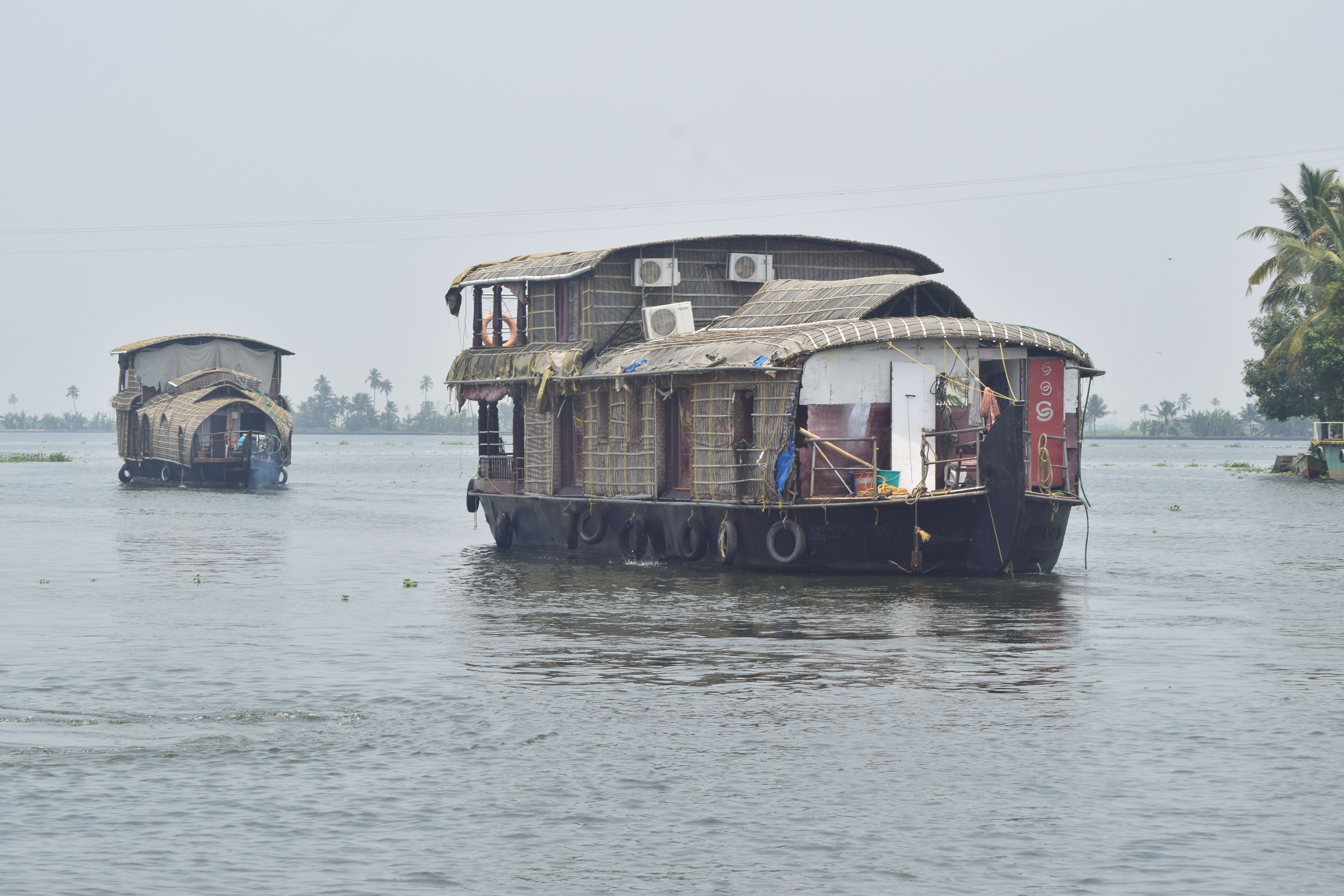 A traditional Kerala kettuvallam houseboat gliding through narrow palm-fringed backwater channels near Alleppey during the monsoon, the water surface reflecting dense tropical vegetation