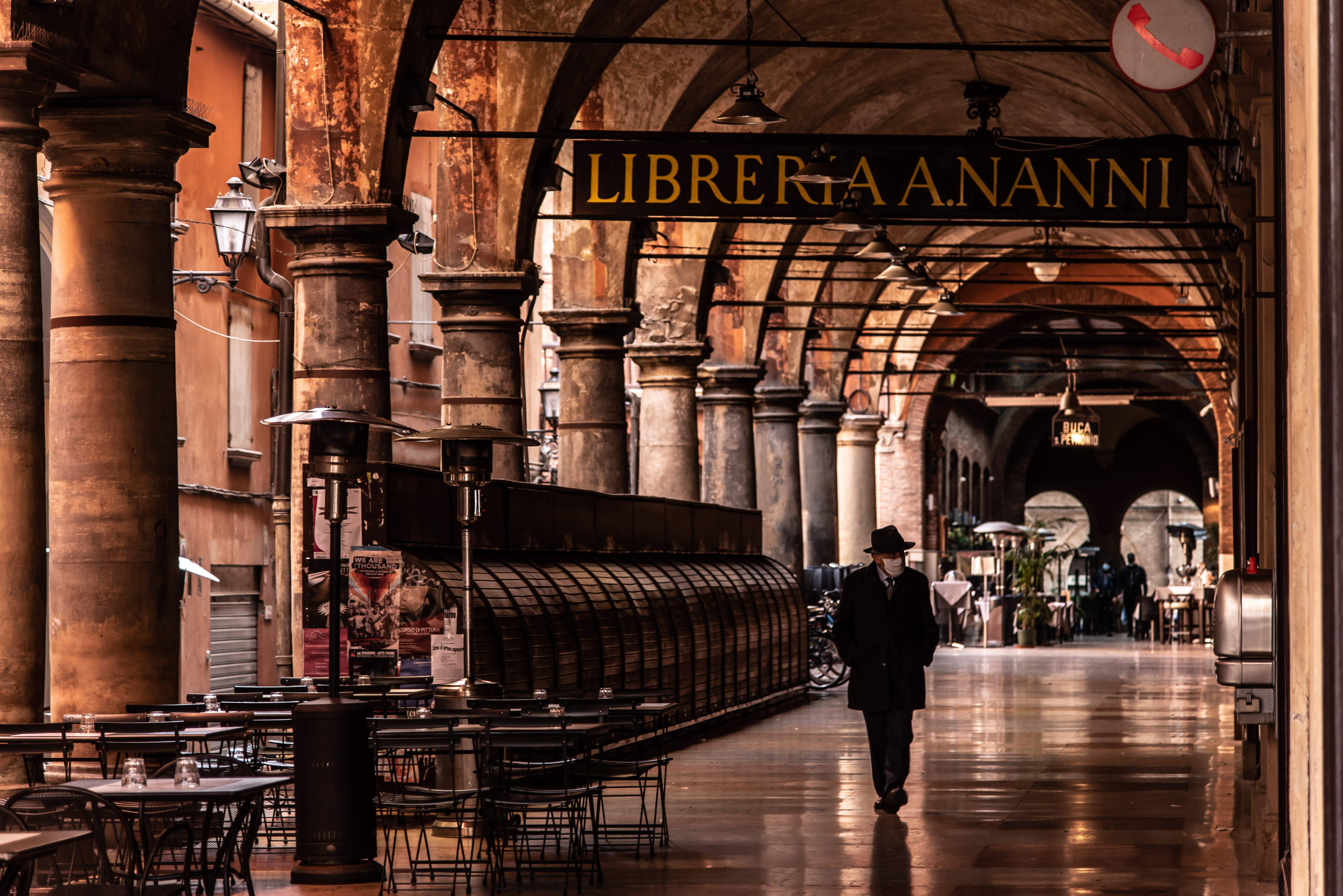 Interior of Mercato di Mezzo in Bologna at morning, with stalls displaying cured meats, wheels of Parmigiano-Reggiano, and fresh pasta under warm ambient light filtering through the covered arcade