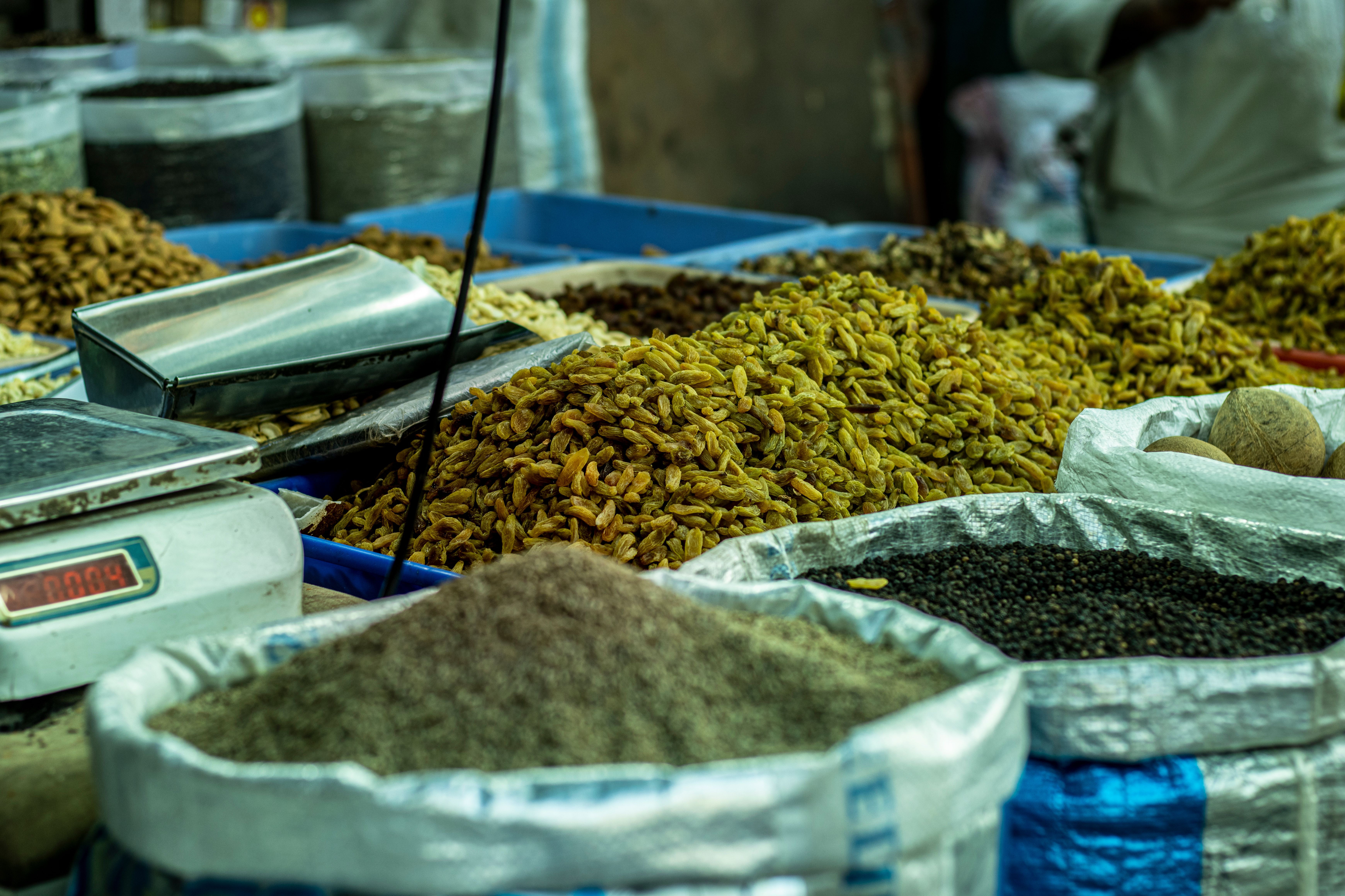 Narrow lane of Old Delhi's Khari Baoli spice market lined with burlap sacks overflowing with colorful dried spices and herbs, traders and buyers moving through the crowded passage