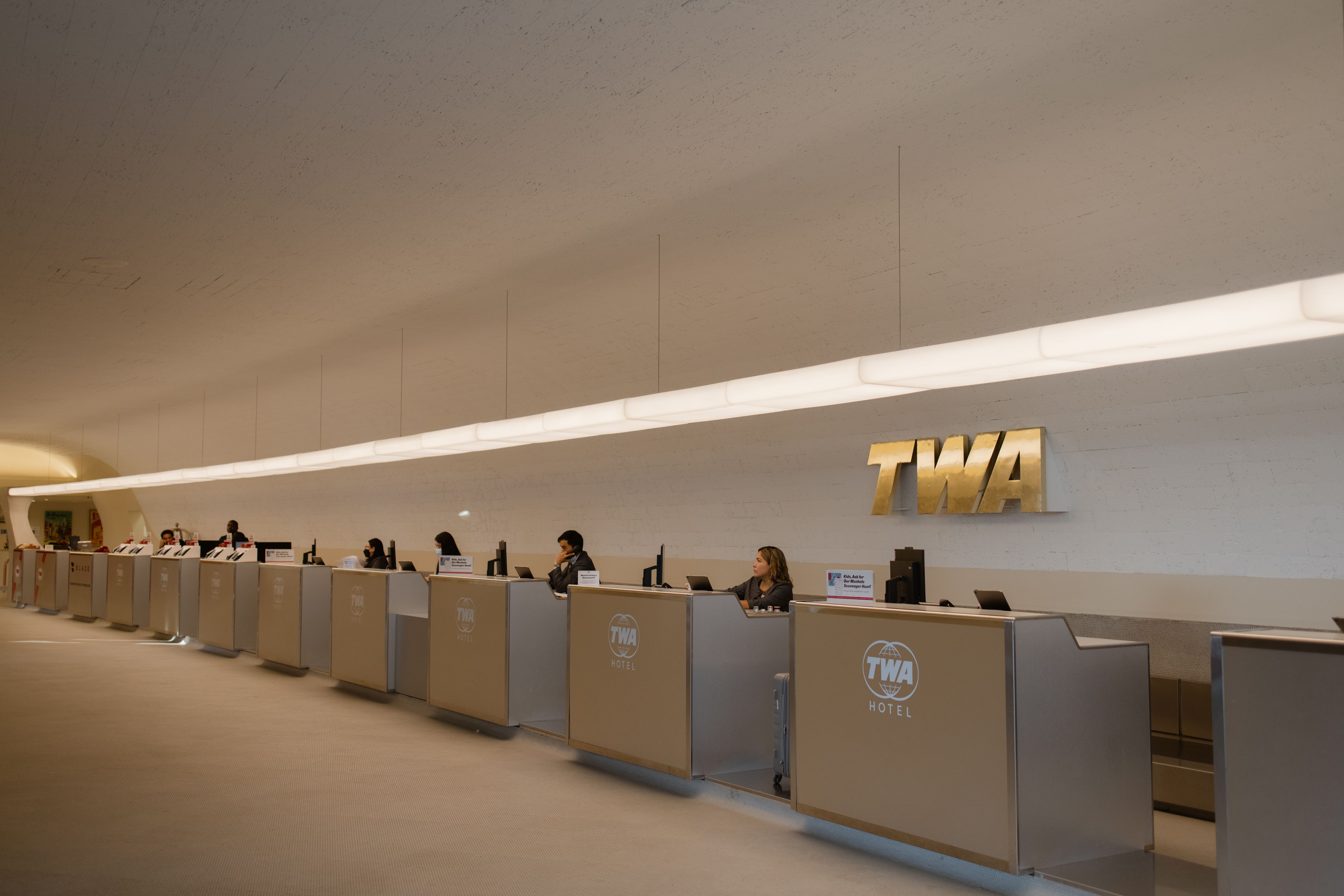 Wide-angle interior of JFK International Airport Terminal 4 bathed in warm golden-hour light, with travelers moving through the departure hall beneath high ceilings and large windows.