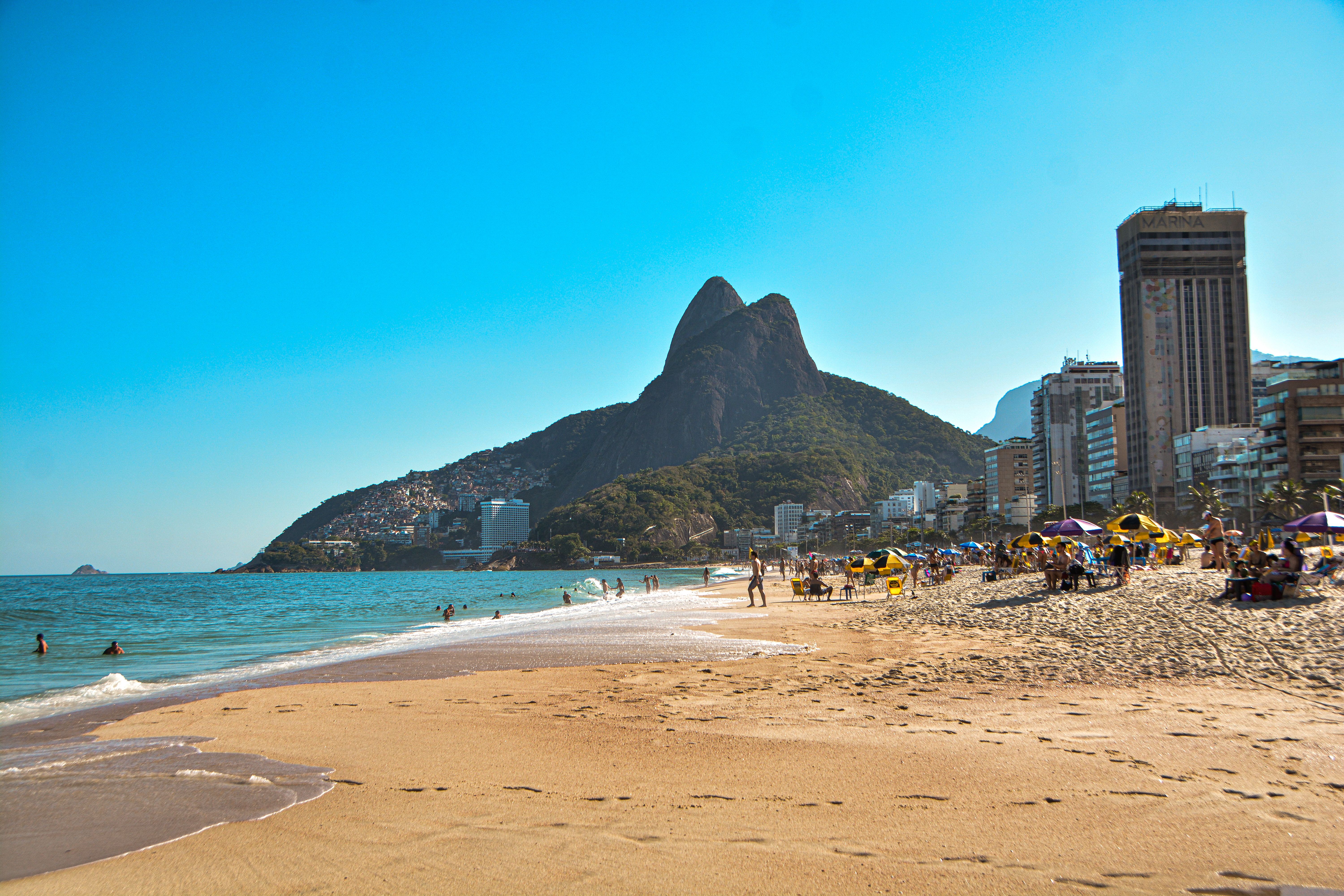 Ipanema beach in Rio de Janeiro with golden sand, colorful beach umbrellas, and the iconic Dois Irmãos twin peaks visible in the background