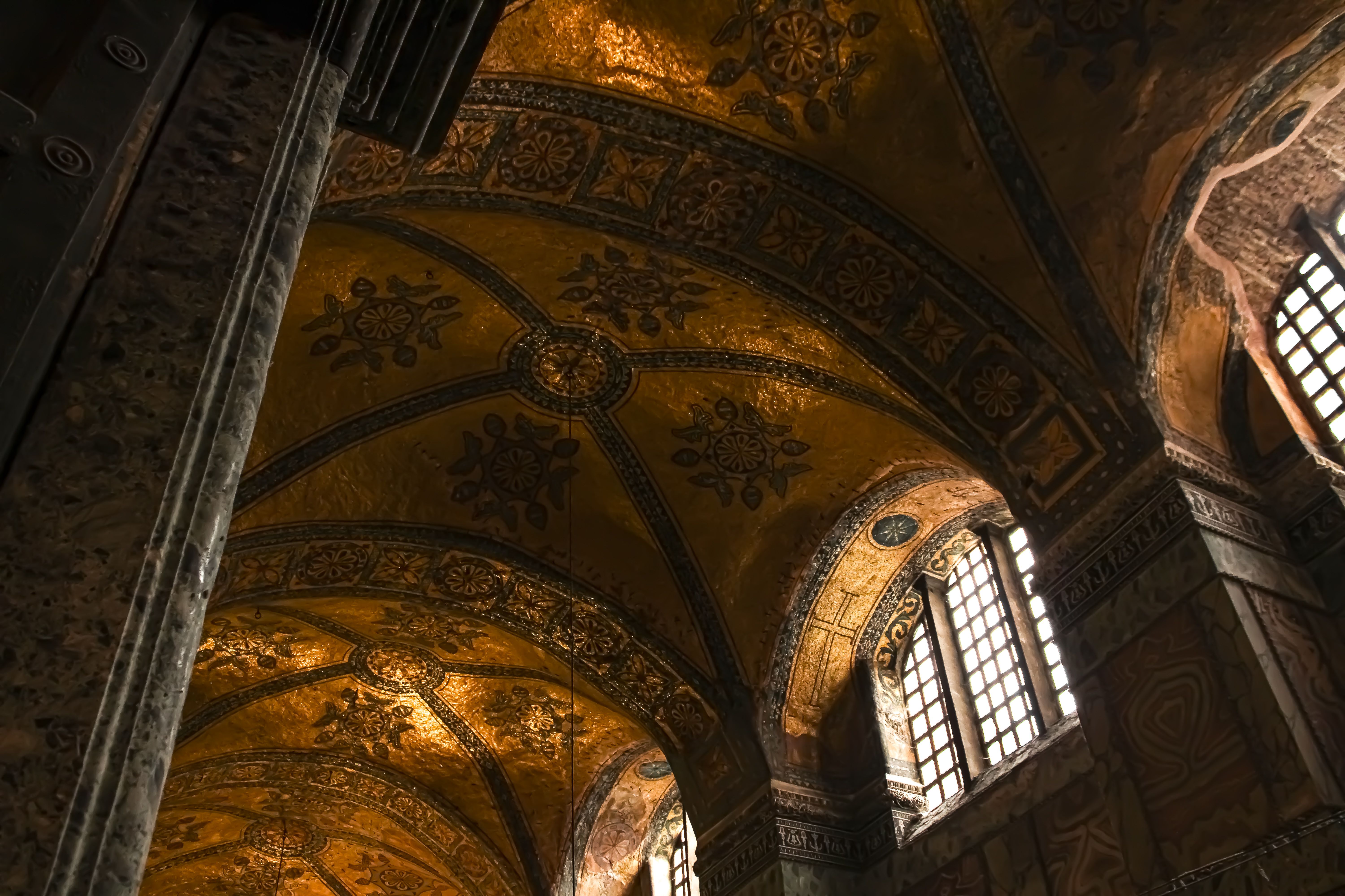 Interior of Hagia Sophia in Istanbul showing the vast Byzantine dome flooded with light, golden mosaics, and towering Ottoman calligraphy medallions below