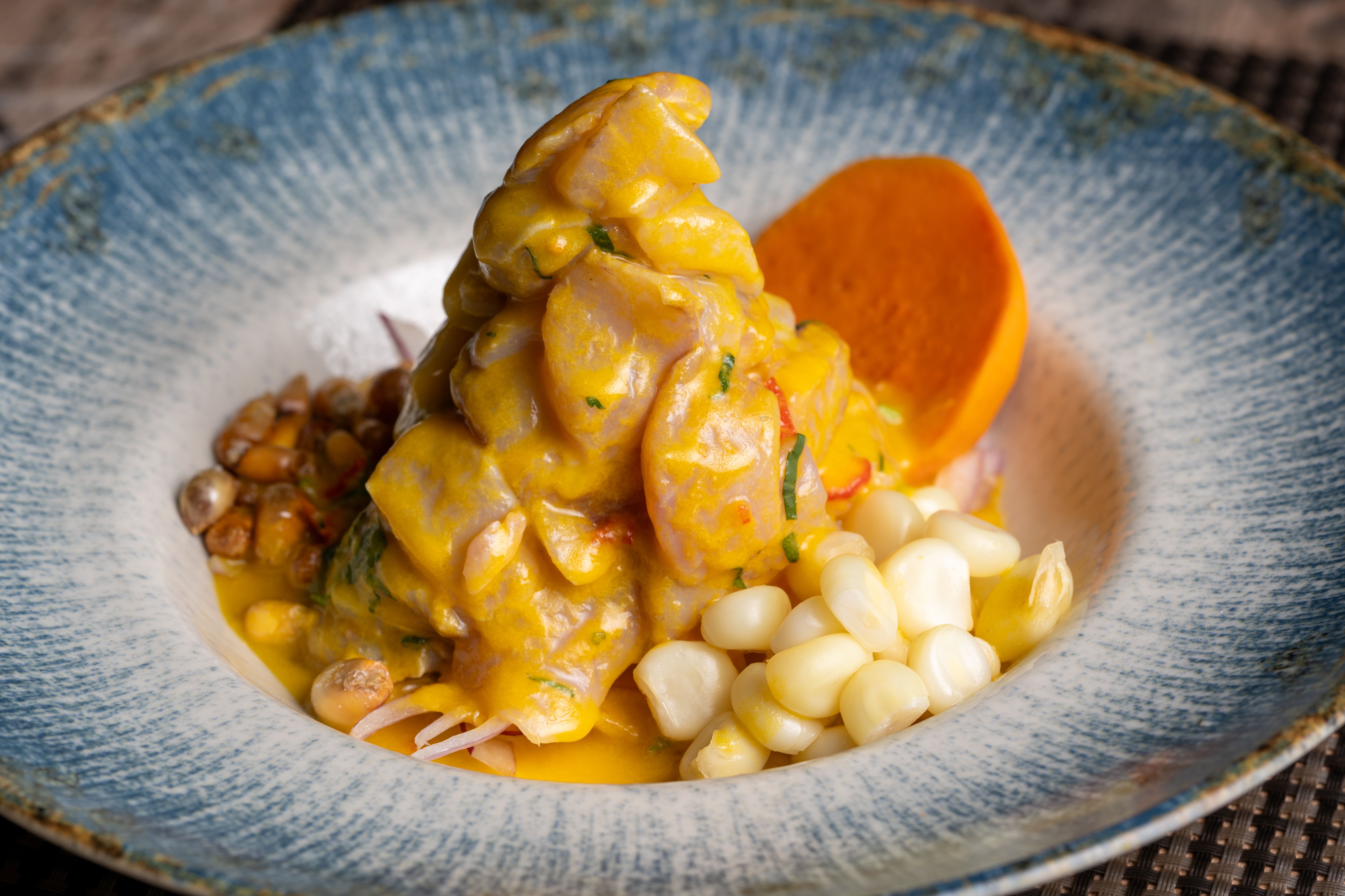 A white ceramic plate of traditional Peruvian ceviche with fresh corvina, thinly sliced red onion, cilantro, and bright yellow ají amarillo peppers, served on a wooden table at a sunlit Miraflores cevichería
