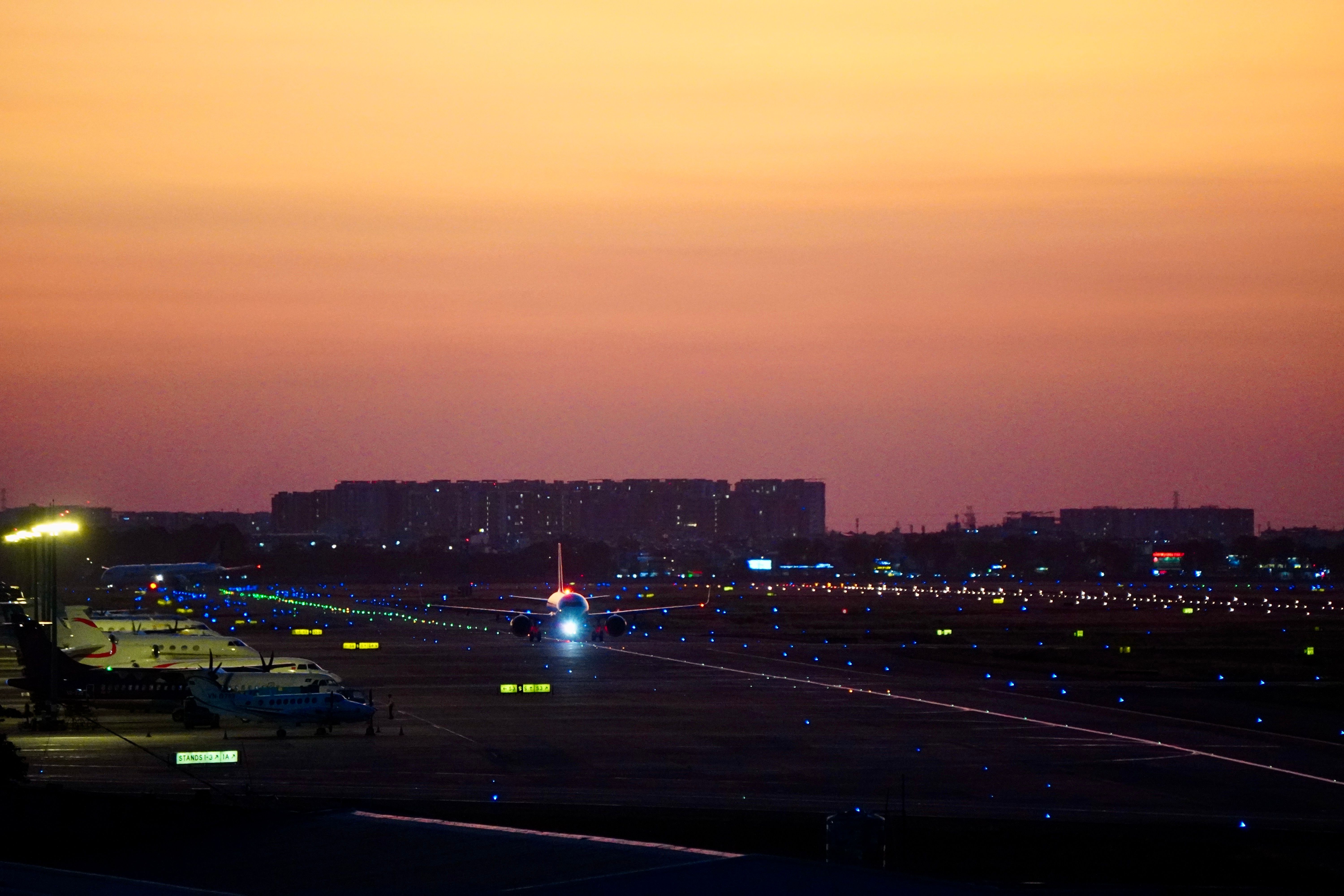 Detroit Metropolitan Wayne County Airport terminal exterior at twilight in winter, with snow-dusted tarmac and warm terminal lights glowing against a deep blue sky