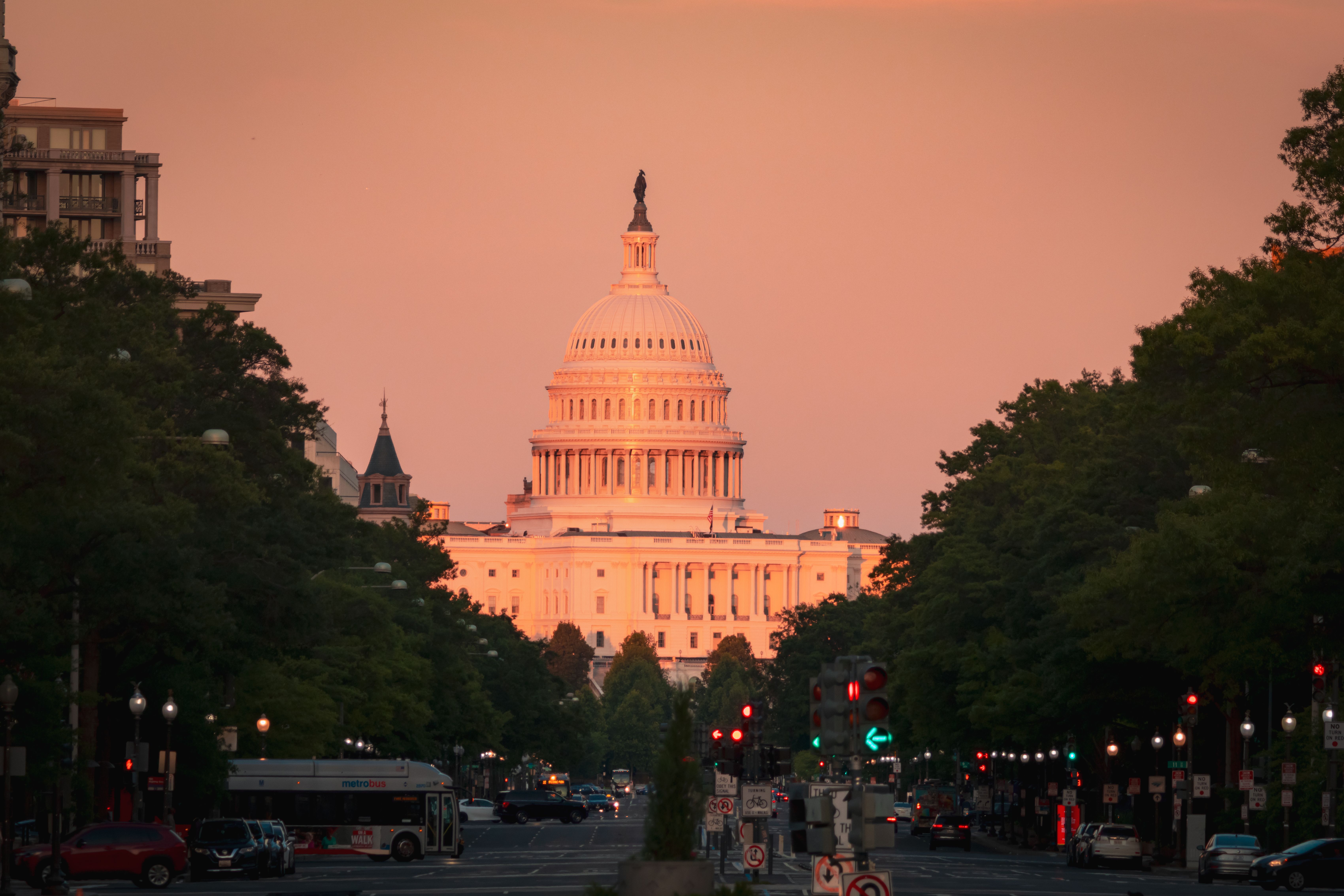 Twilight view of Washington DC's Pennsylvania Avenue with illuminated hotel facades and the Capitol dome visible in the distance