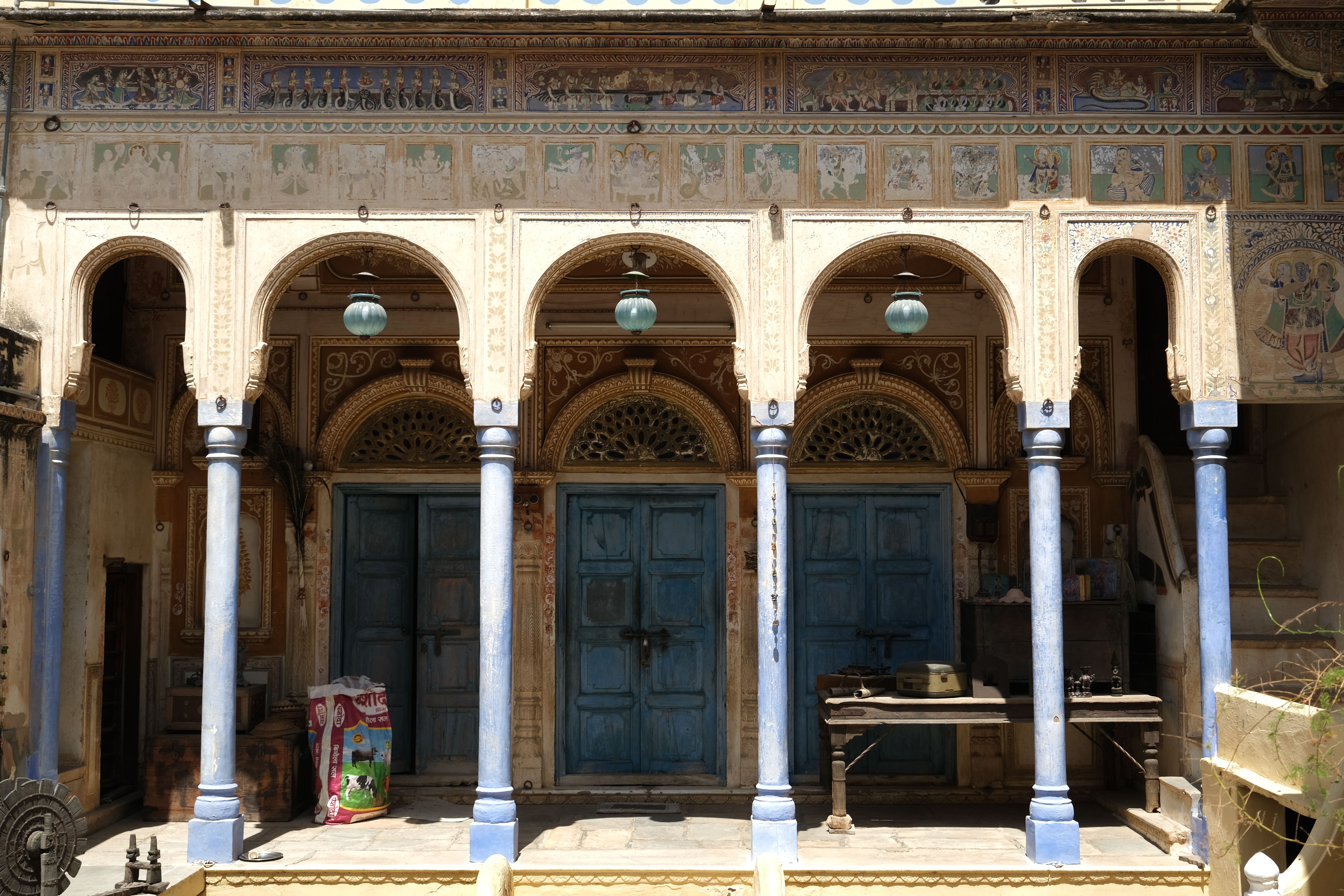 Ornate hand-painted murals covering the interior courtyard walls of a historic haveli in the Shekhawati region of Rajasthan, depicting figures, animals, and geometric patterns in vivid pigments