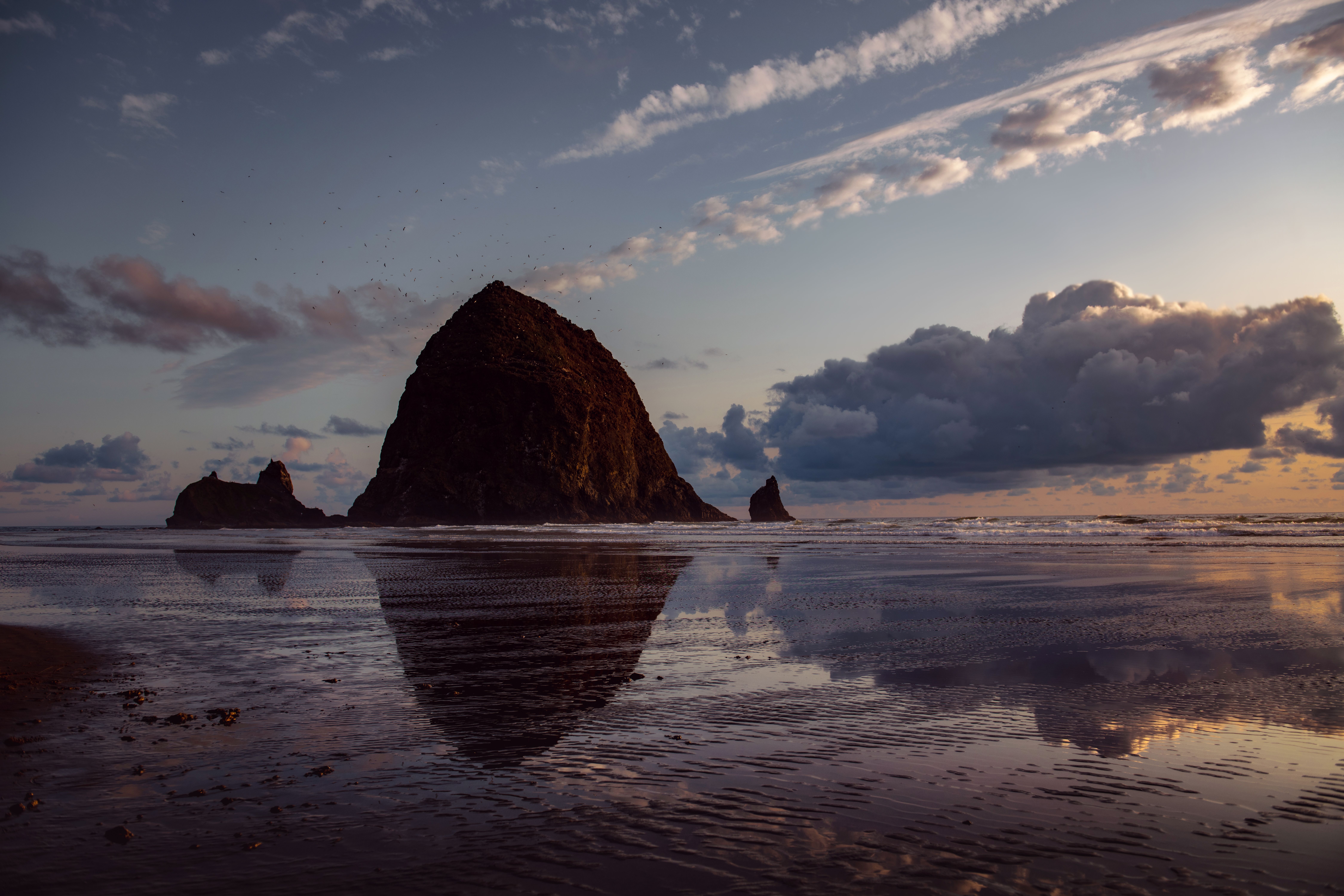 Haystack Rock standing in the surf at Cannon Beach, Oregon, with tide pools at its base and the Pacific Ocean stretching to the horizon