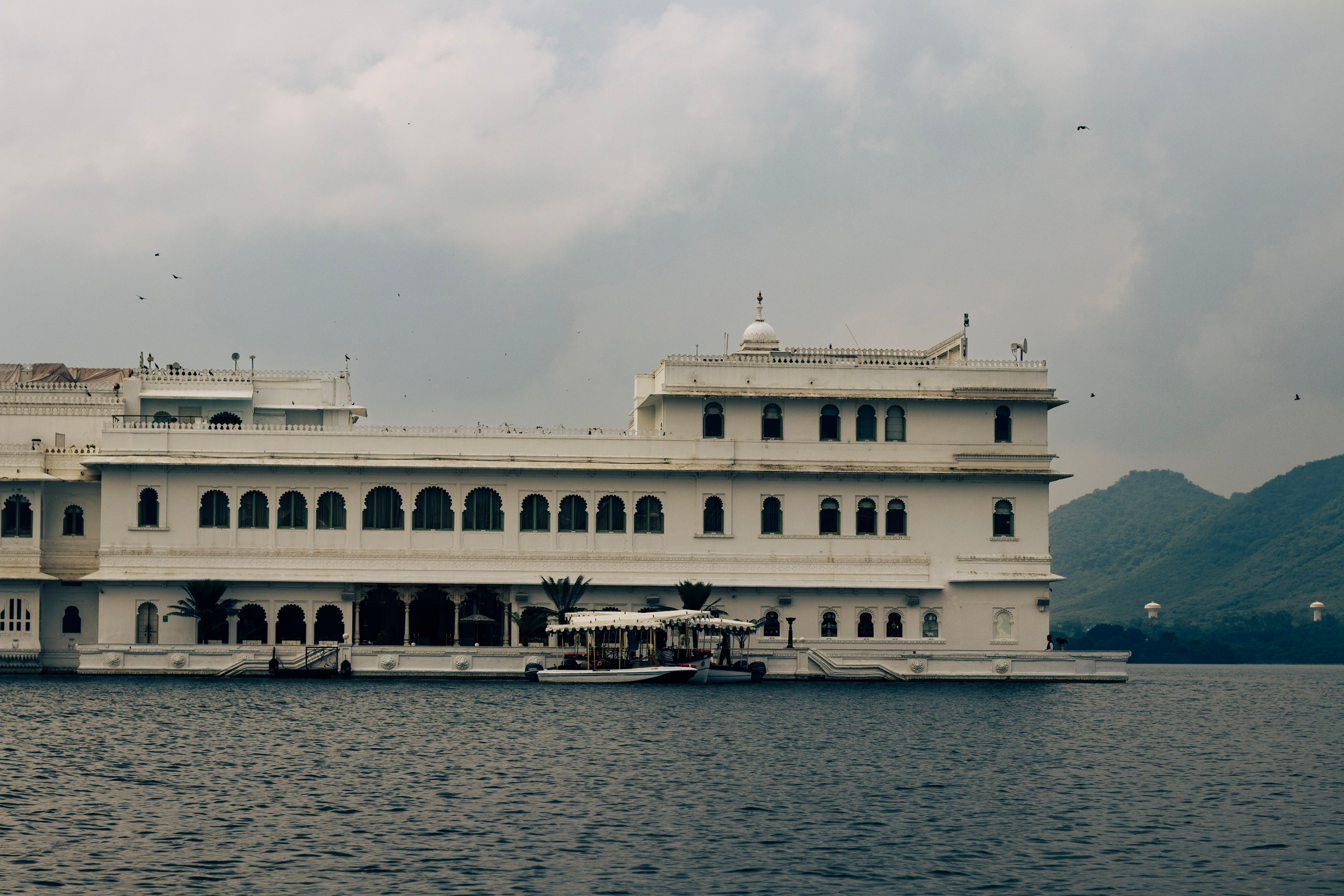 The white marble Taj Lake Palace hotel appearing to float on the glassy surface of Lake Pichola in Udaipur, Rajasthan, with the Aravalli Hills visible in the background at dusk