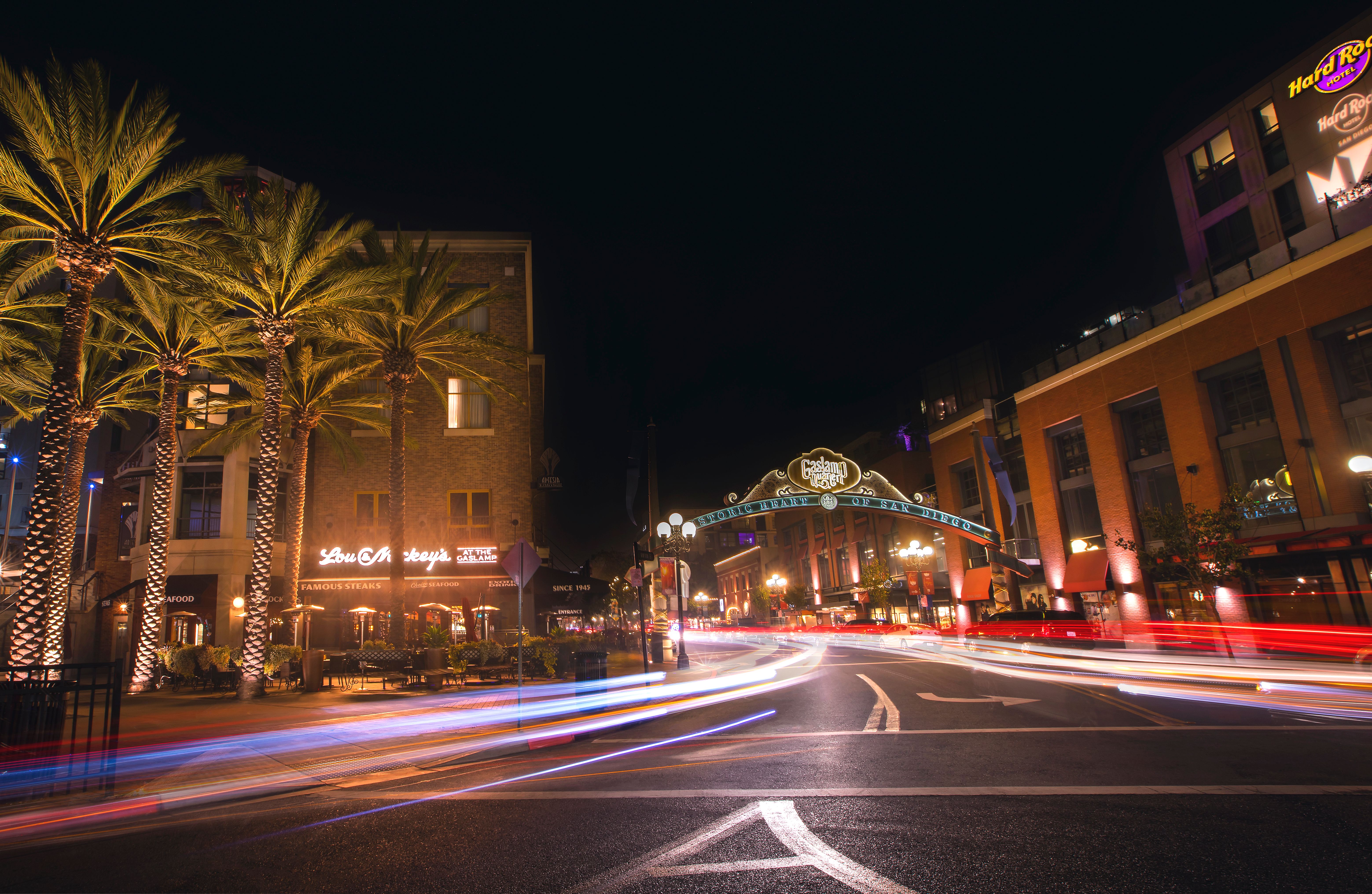 Golden hour light washing over the historic Victorian architecture of San Diego's Gaslamp Quarter, with hotel marquees and palm-lined streets stretching toward the bay