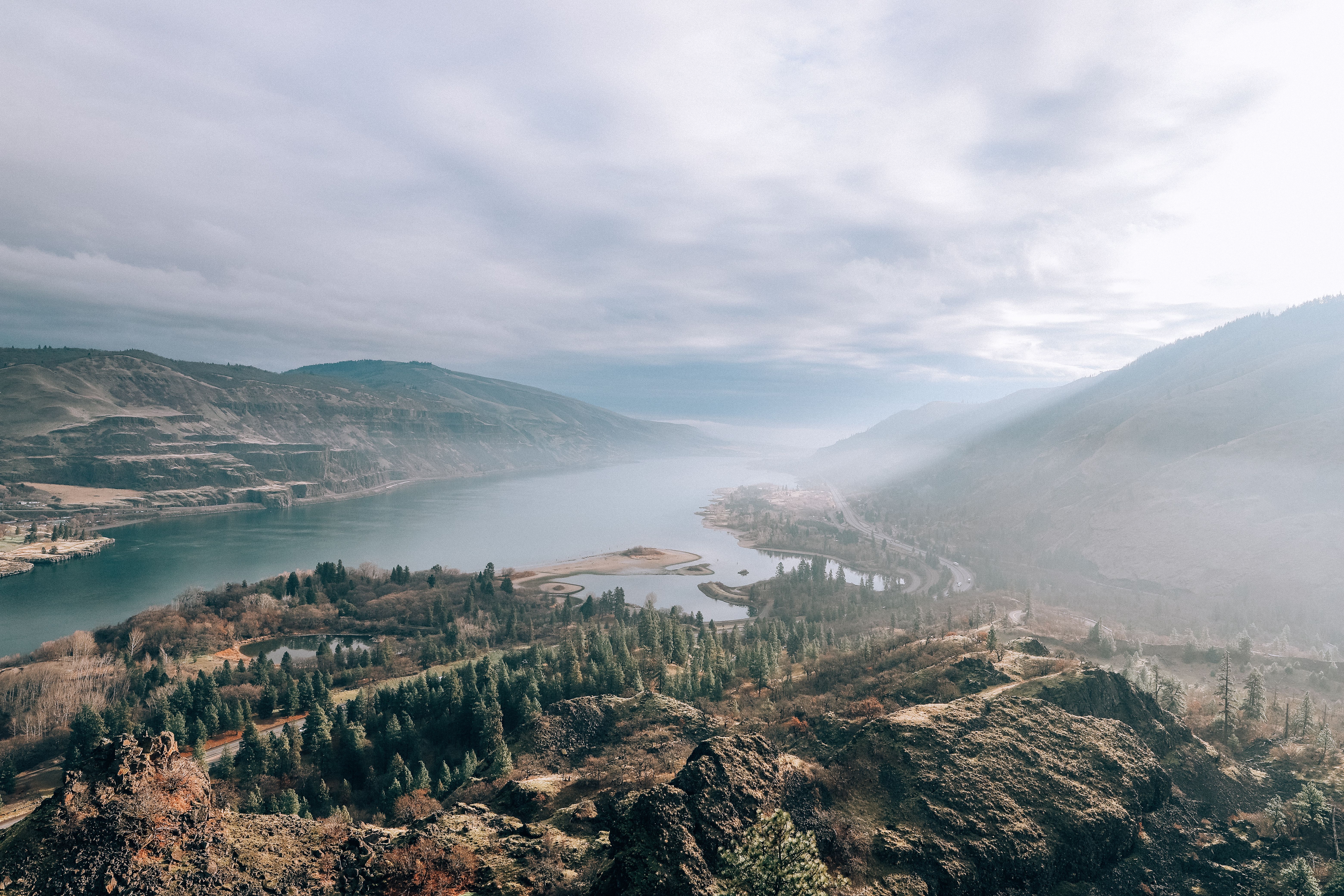 Aerial view of the Columbia River Gorge at golden hour, with mist rising from the river and basalt cliffs glowing amber in morning light