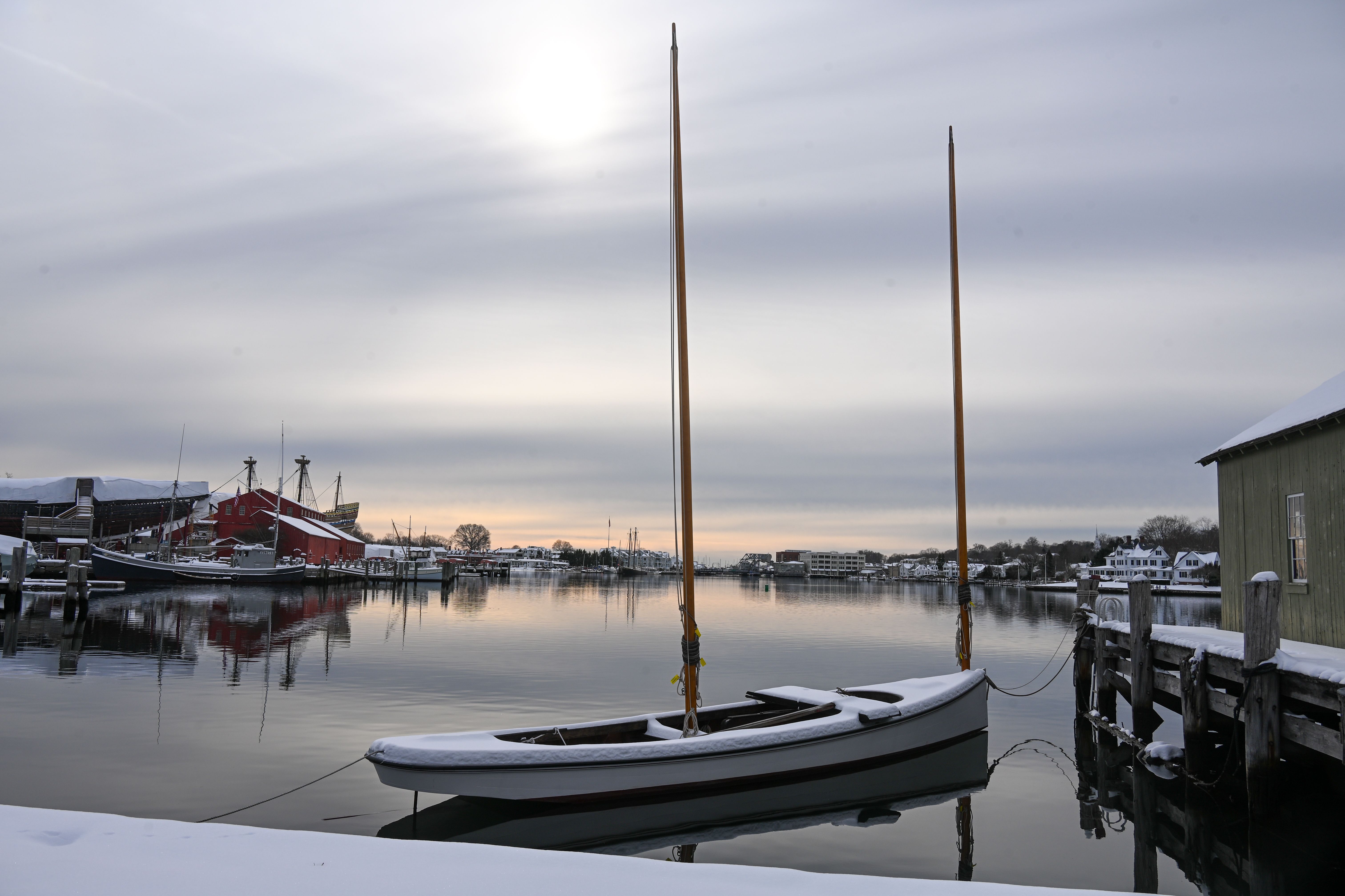Wooden lobster boats moored at the granite wharf of Stonington harbor on Deer Isle, Maine, with morning fog drifting over calm dark water at dawn
