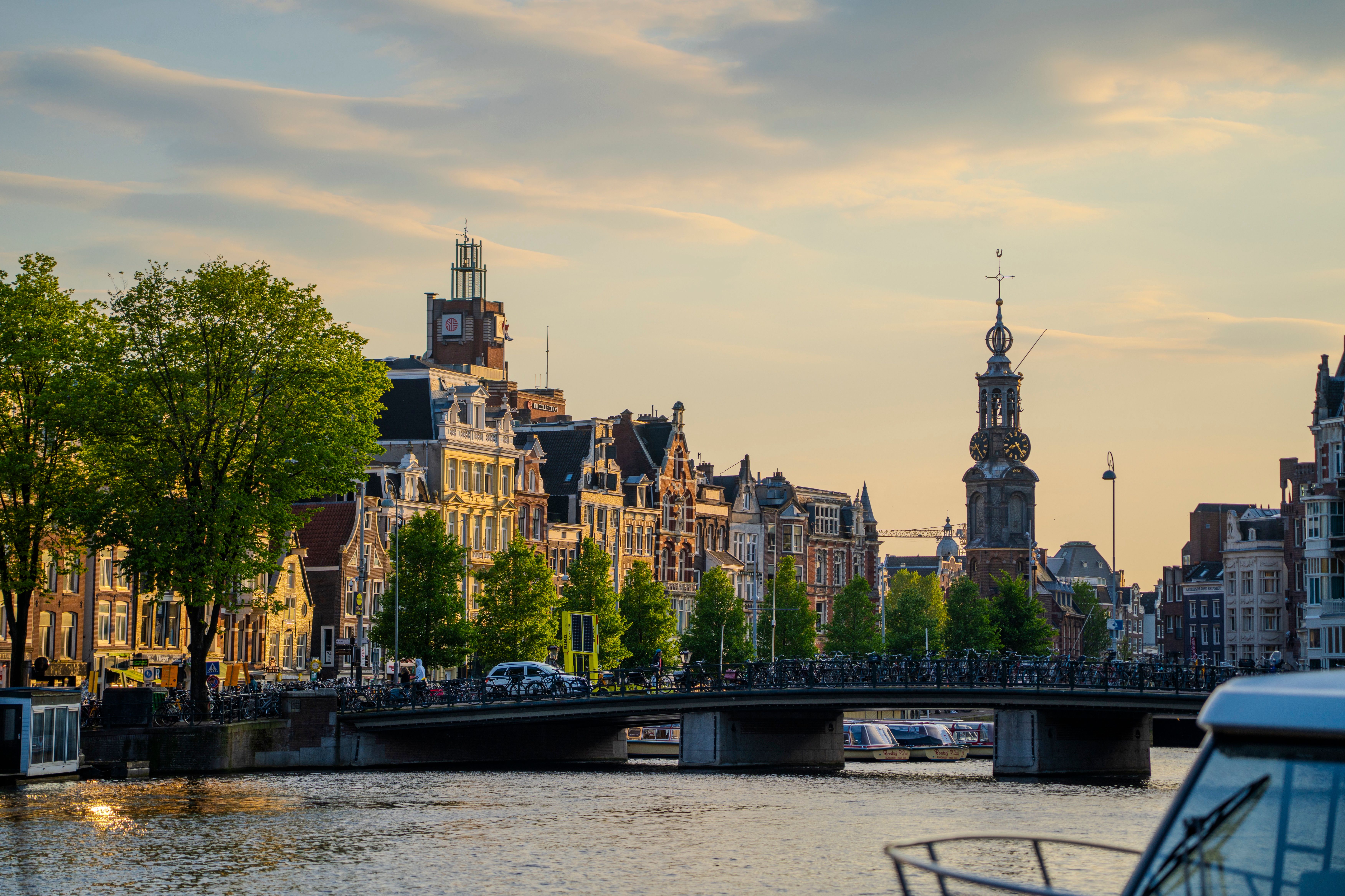 Golden hour light reflecting off Amsterdam's historic canal houses, the city where Booking.com is headquartered, with narrow bridges and bicycles lining the waterfront