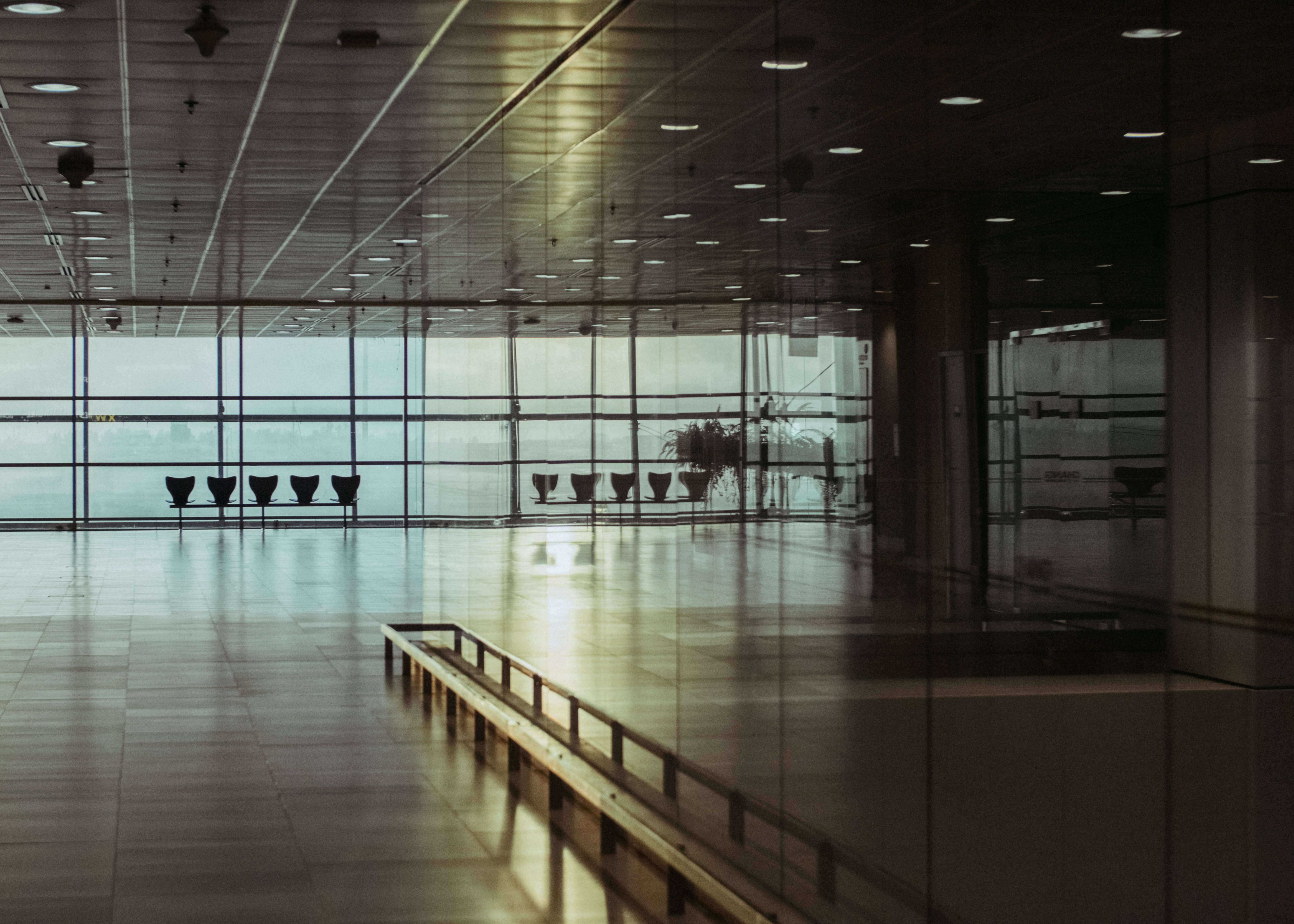 Wide-angle cinematic view of Dallas/Fort Worth International Airport Terminal D interior, showing the lower-level baggage claim area with carousels, dramatic overhead lighting, and the vast architectural expanse of the terminal hall