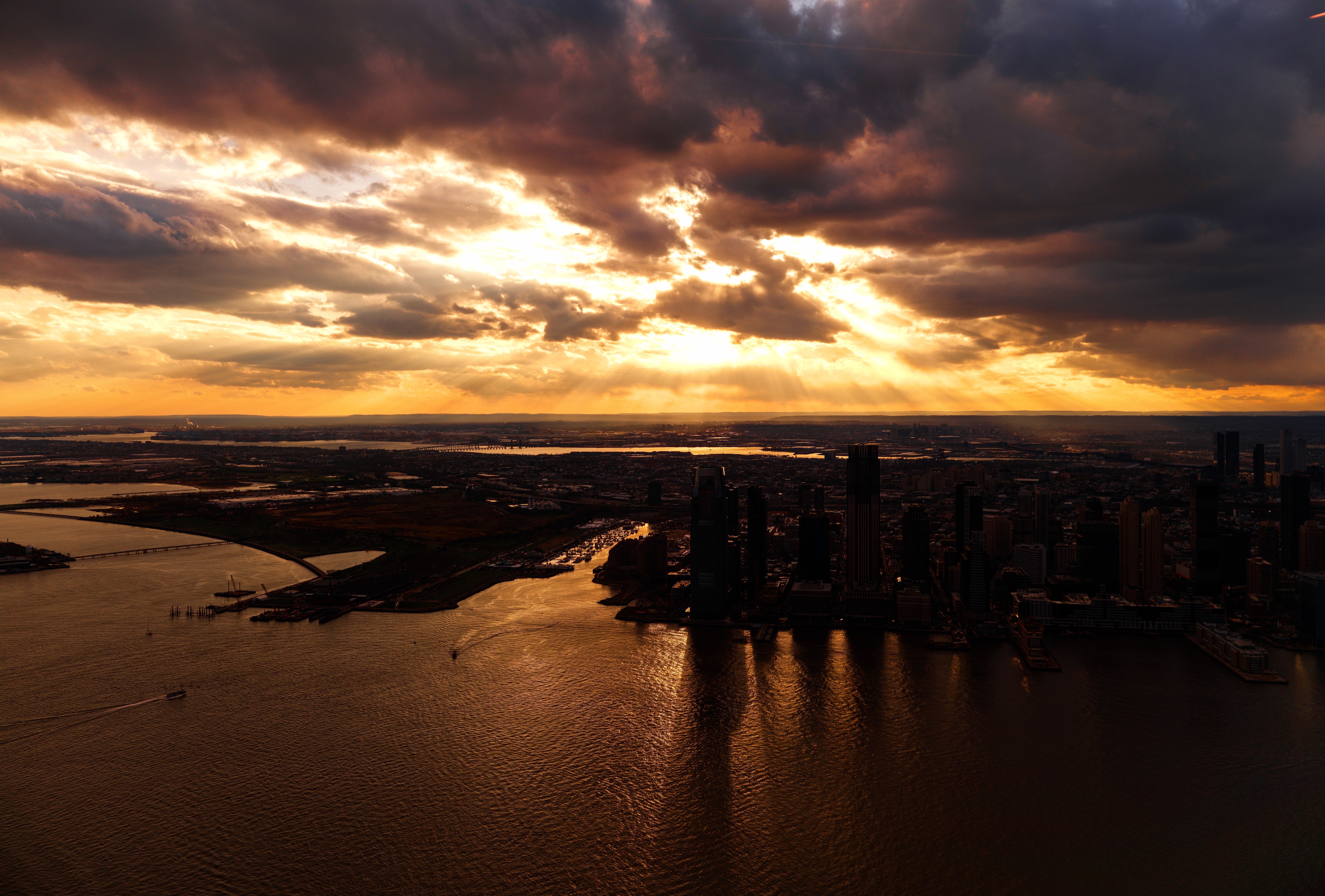 Dramatic golden hour view of the Manhattan skyline with the East River in the foreground, skyscrapers glowing in warm late-afternoon light