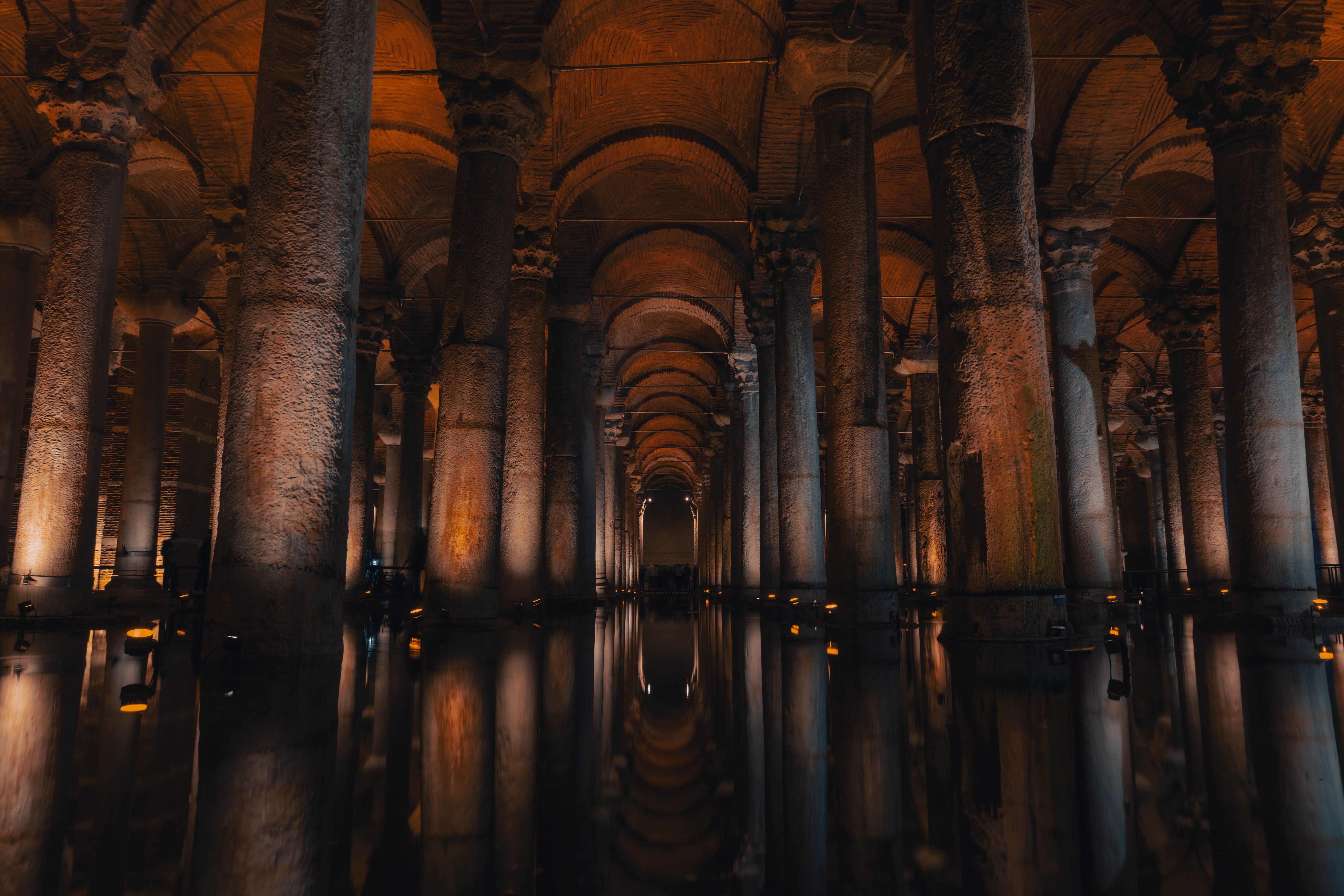 The underground Basilica Cistern in Istanbul with rows of marble columns illuminated by amber light reflecting on the dark water below