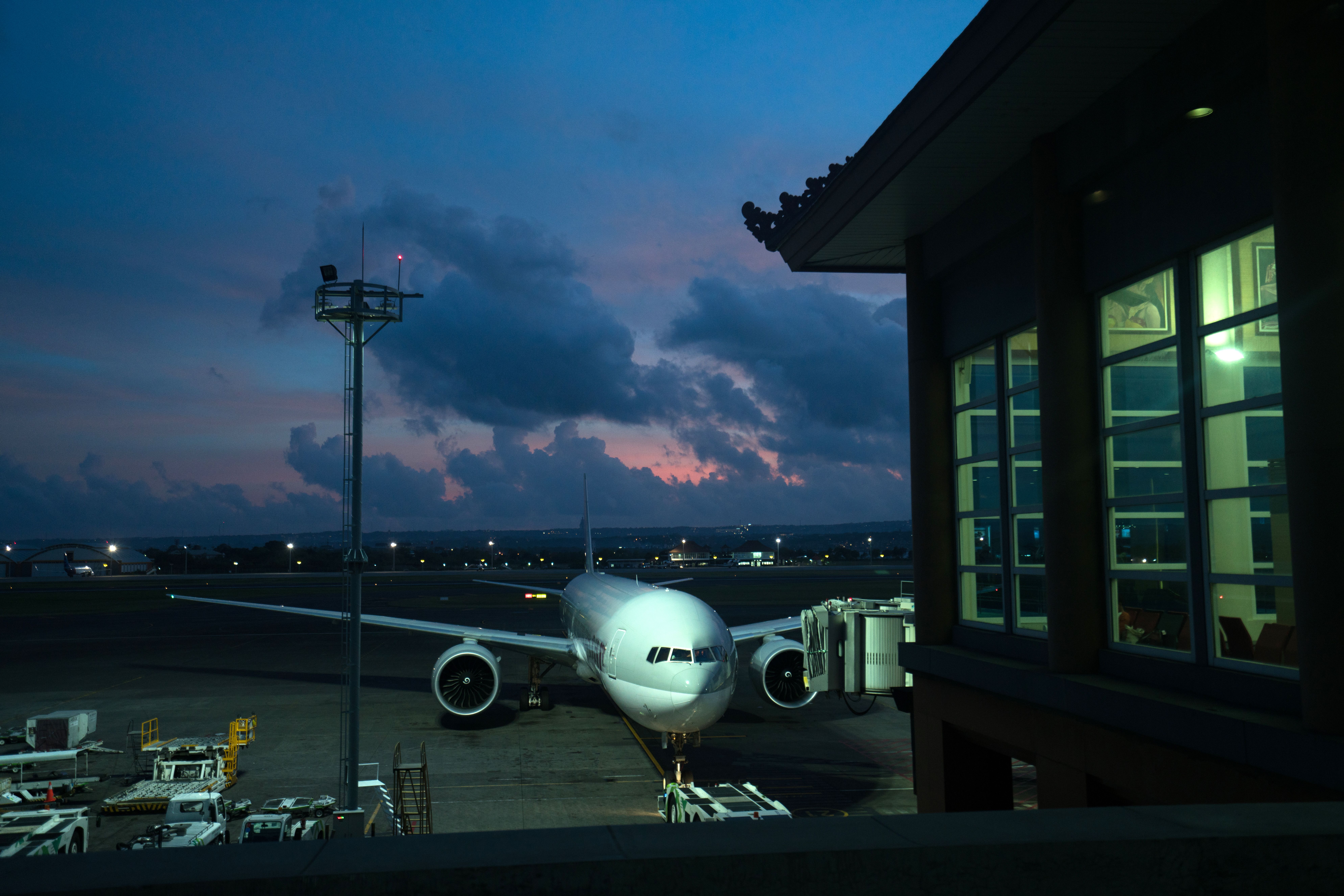Wide-angle cinematic view of the interior concourse at George Bush Intercontinental Airport at dusk, with gate seating, departure boards, and floor-to-ceiling windows casting long golden light across the terminal floor