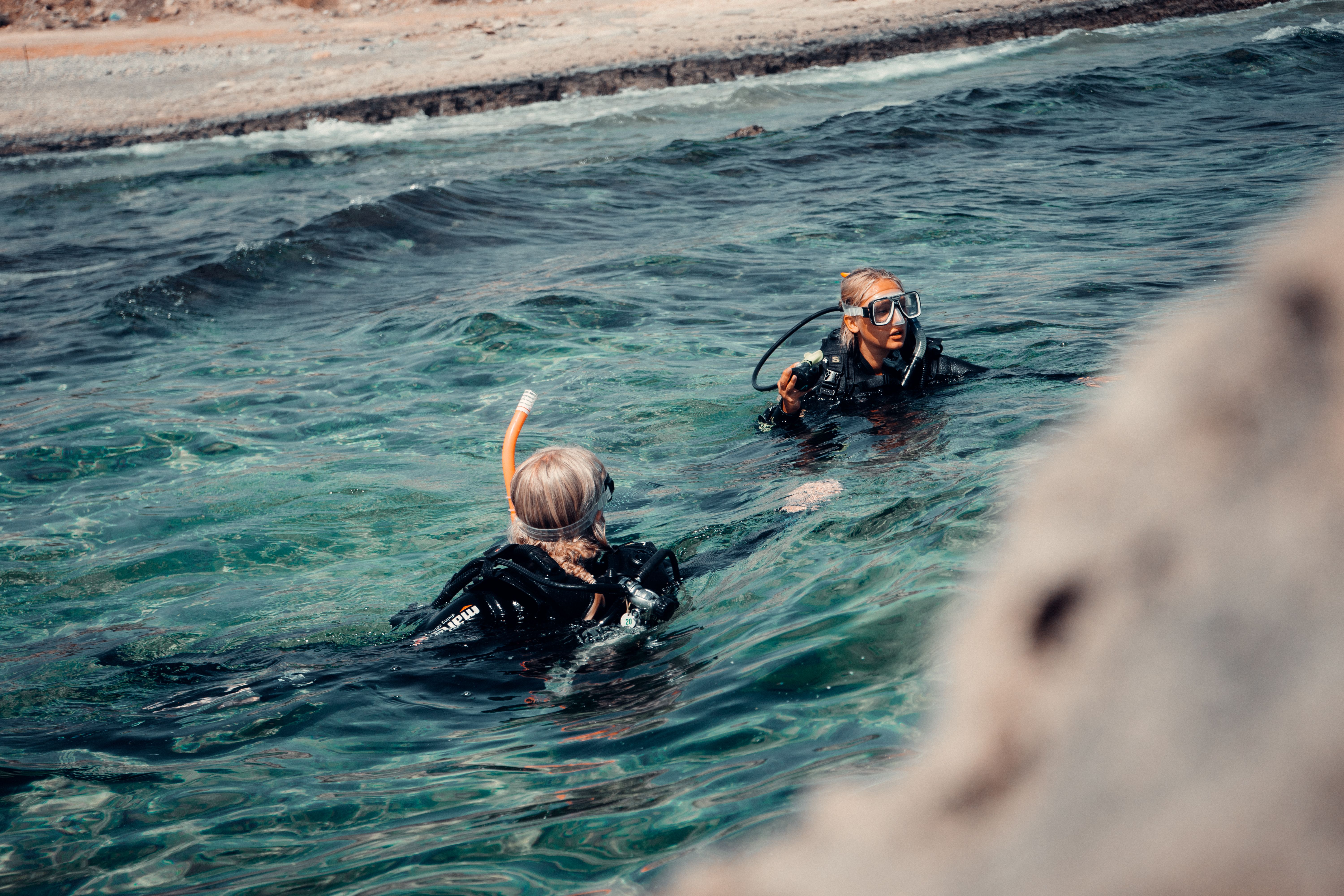 Scuba diver descending through clear blue tropical water with coral reef below