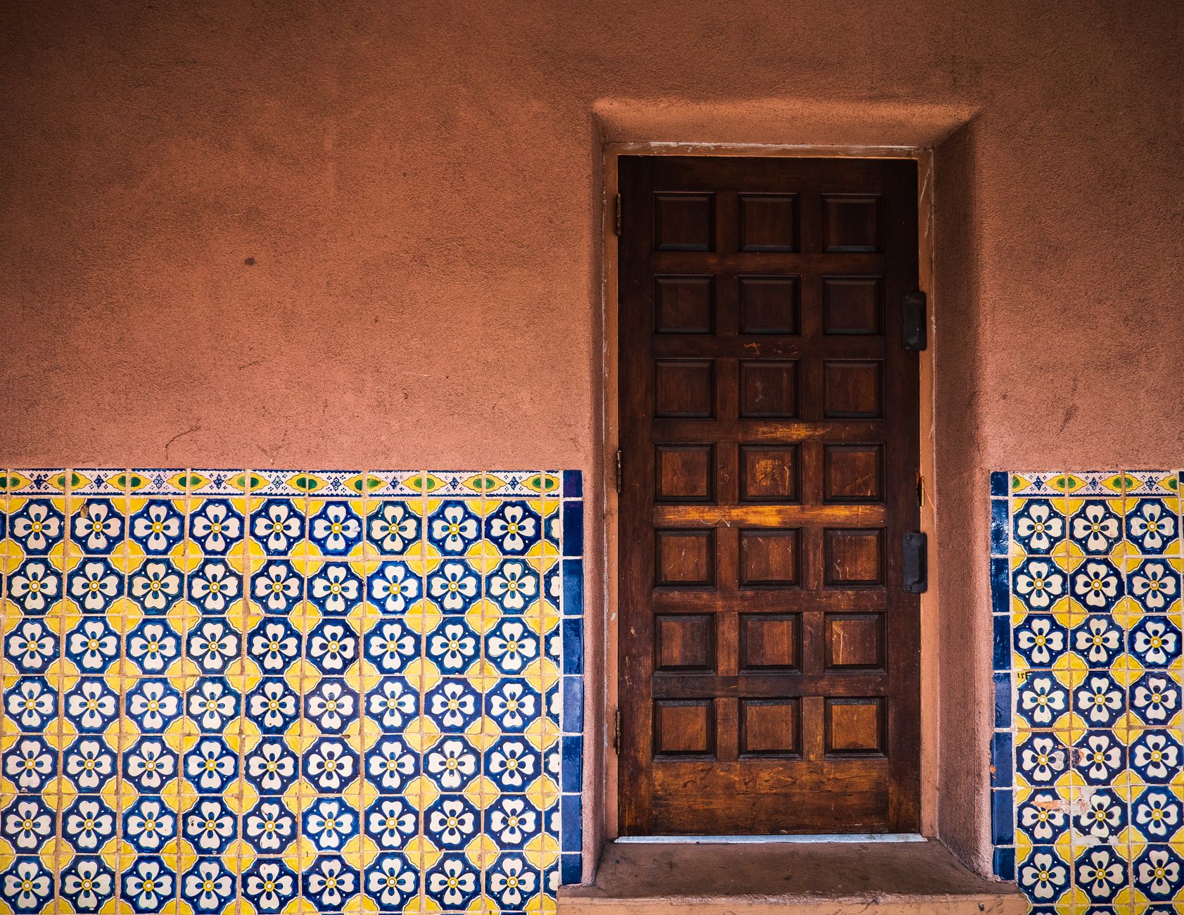 Rustic wooden door with vibrant patterned tiles in Santa Fe, reflecting Southwestern charm.
