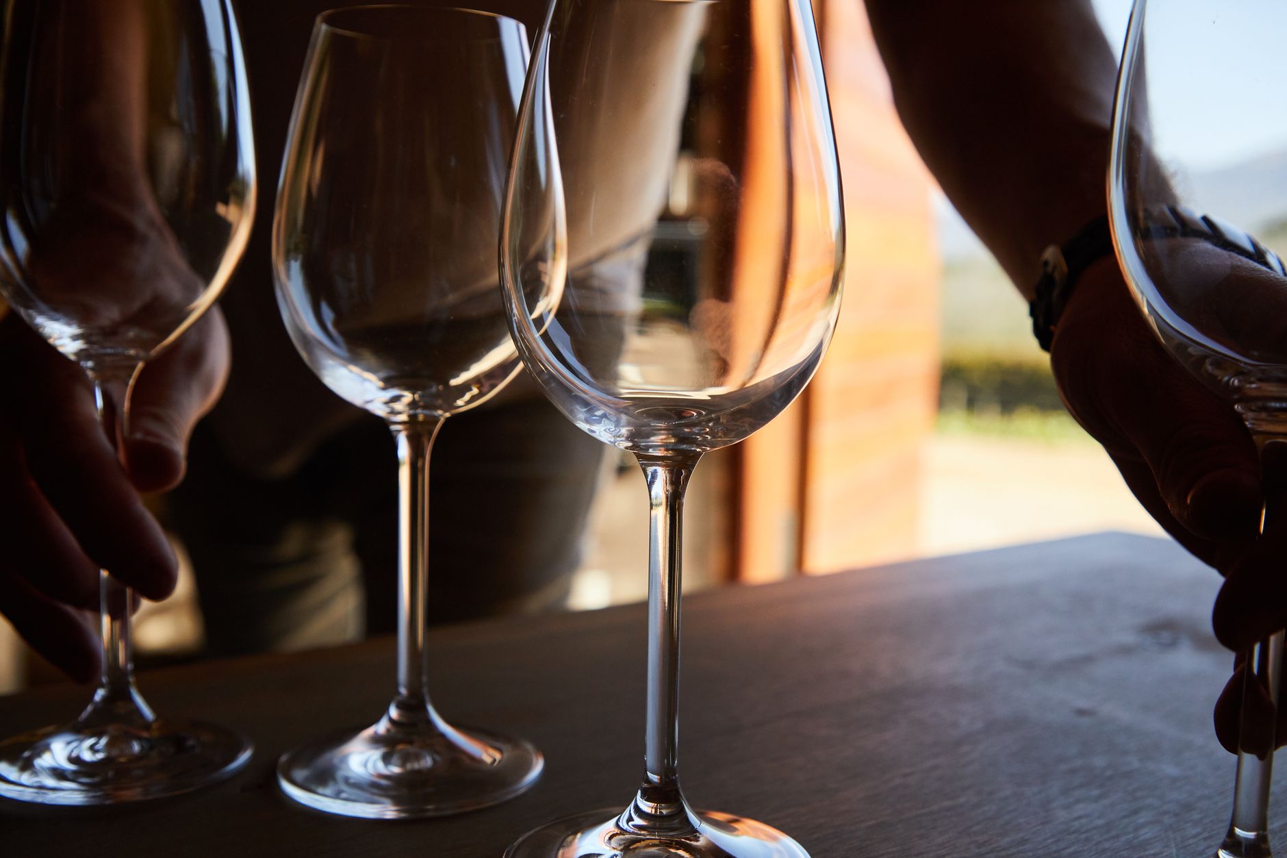Hands arranging wine glasses on a table with natural light.