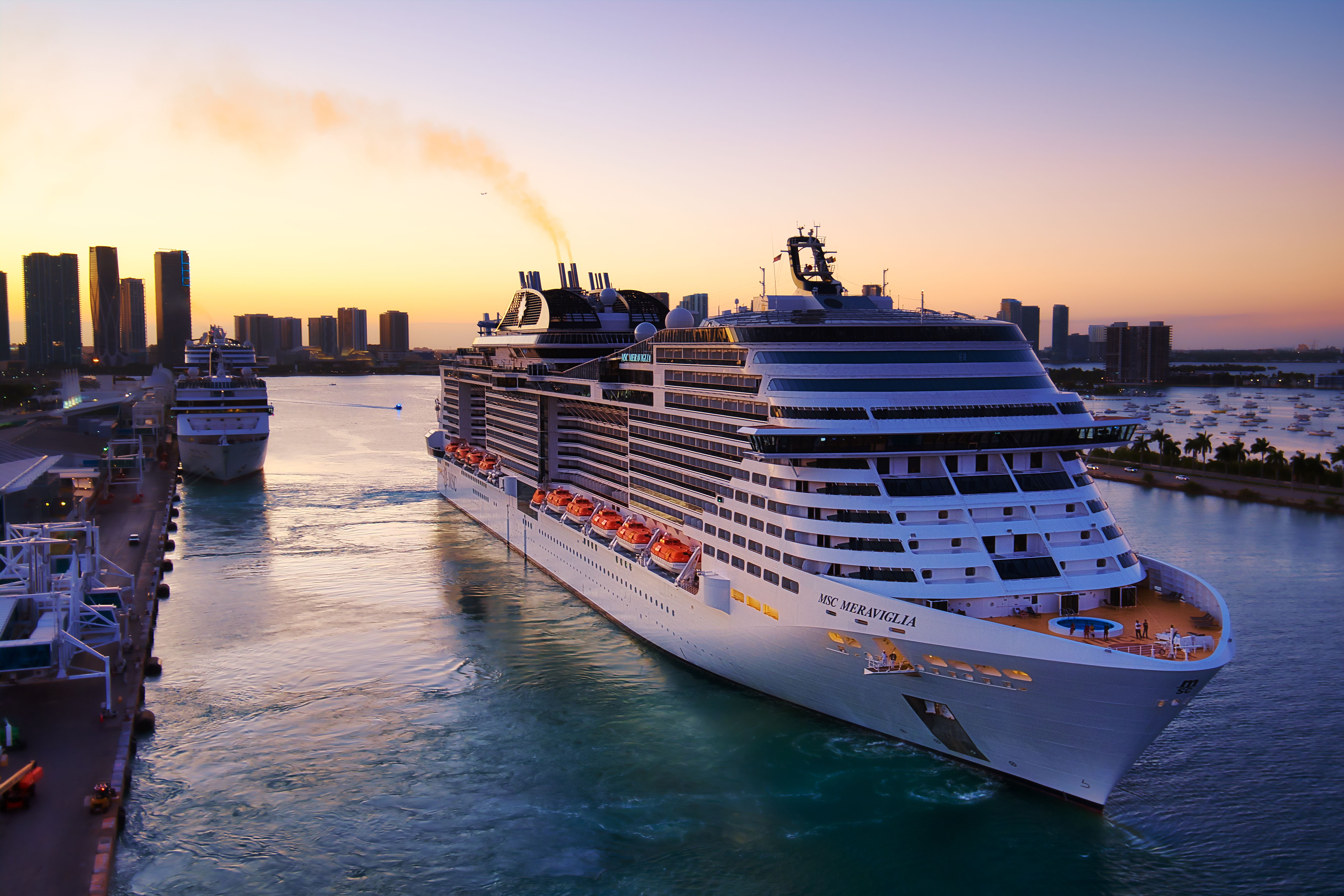 Golden hour aerial view of the Port of Miami cruise terminal with large cruise ships docked along the waterfront, city skyline in the background