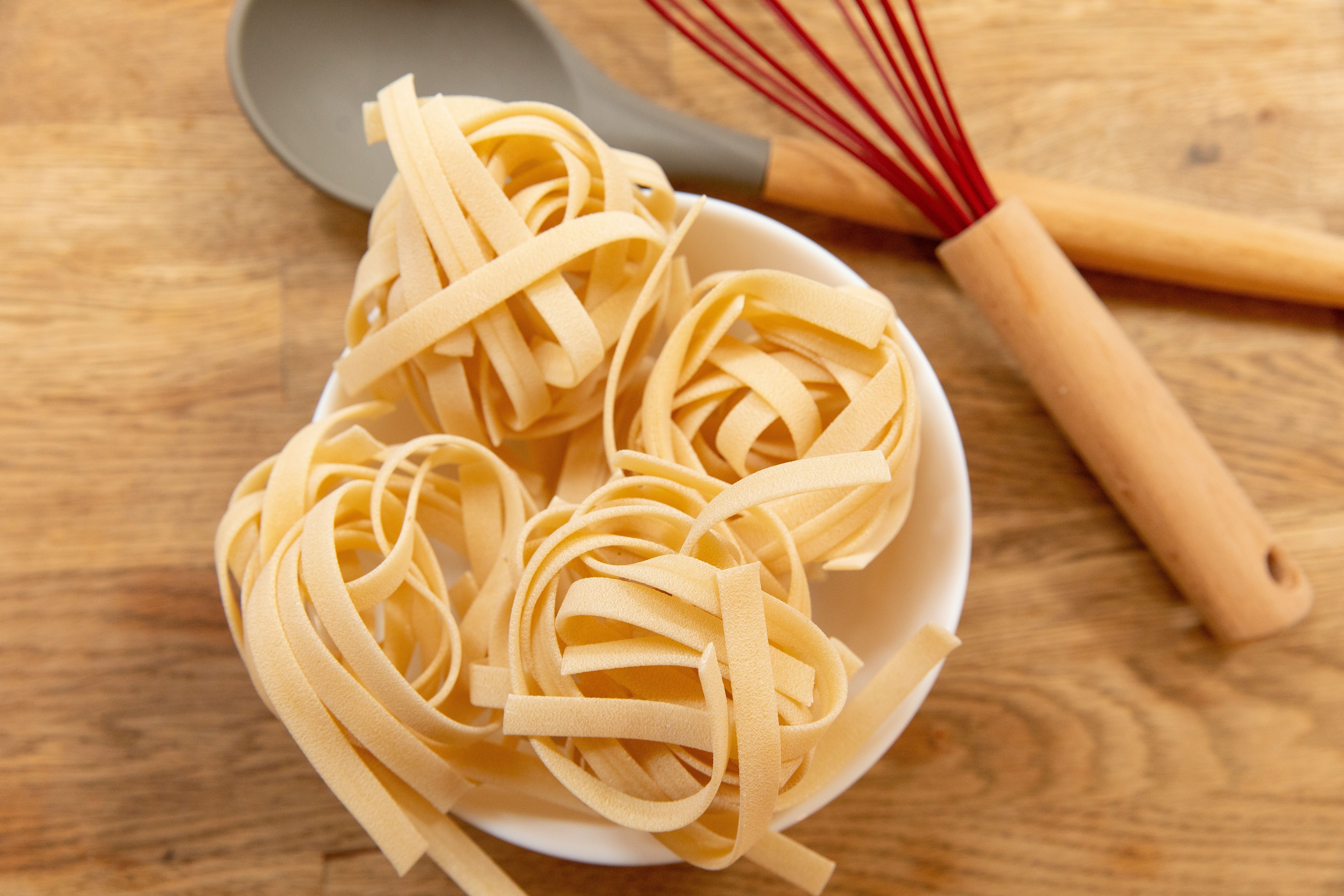 A bowl of handmade tagliatelle al ragù at a Bologna trattoria, the wide fresh egg pasta ribbons coated in a rich, slow-cooked meat sauce, served on a simple ceramic plate on a wooden table