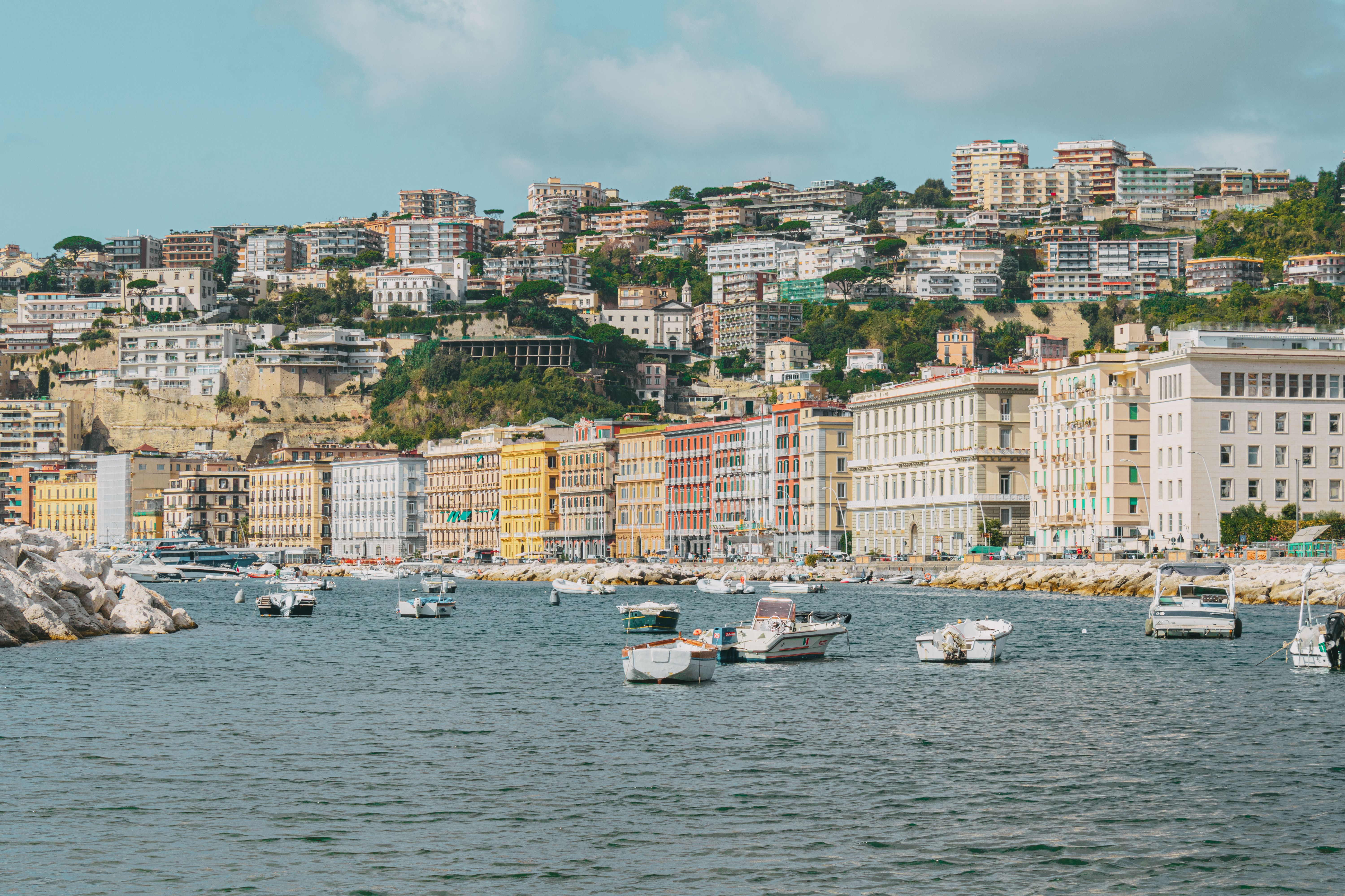 Golden hour view of the Port of Naples waterfront with cruise ships docked and Vesuvius visible in the distance against a warm amber sky